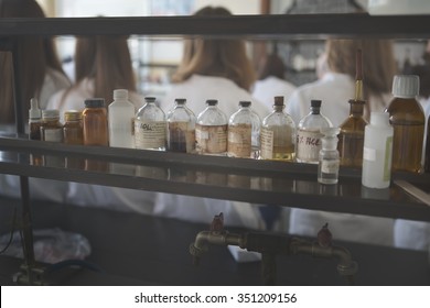 Chemicals And Laboratory Utensils.Vintage Pharmacy Bottles On Wooden Board.Chemical Bottles For Use On Chemistry Class.Safe Chemicals For Organic Chemistry Lab.Students Blurred In The Background