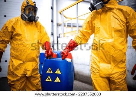 Chemicals production factory. Experienced workers fully protected in gas mask carrying hazardous and toxic waste in chemical plant.