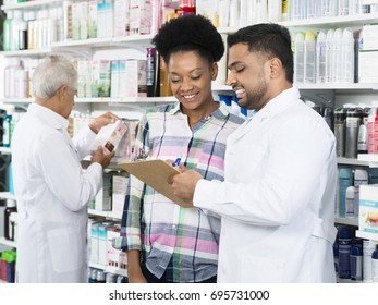 Chemist Explaining Prescription To Customer In Pharmacy