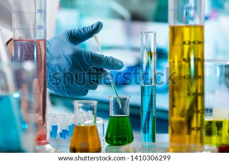 Chemist mixing fluids with a pipette in the research laboratory / hand of researcher with pipette measuring sample in beaker of liquids in the chemical lab  