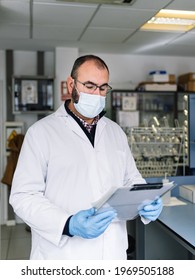 Chemist Reviewing A Work Report. Lab Technician With Protective Mask Looking At Technical Data. Photography Vertical