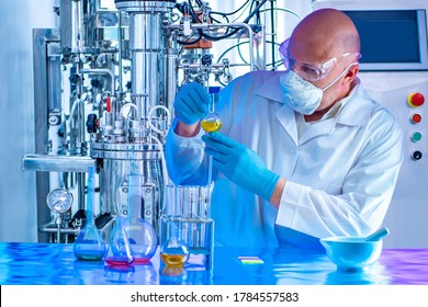 Chemist with a test tube on the background of a laboratory fermenter. Observation of the fermentation process. Laboratory equipment. Experiments in the field of pharmaceuticals. Microbiology.