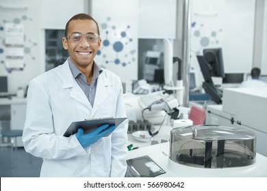 Chemistry is his passion. Handsome young African male scientist wearing protective glasses smiling happily holding his clipboard working at the lab professionalism occupation job people copyspace - Powered by Shutterstock