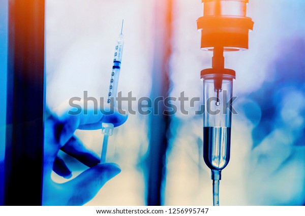 Chemotherapy drug medical holding hypodermic\
syringe needle injection iv bag fluid intravenous drop saline drip\
hospital room concept treatment  palliative care.selective\
focus.blue light\
background,