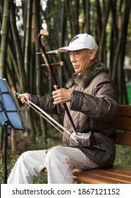 Chengdu, Sichuan, China - 10,10,2020
An Older Chinese Man Sitting On A Bench And Playing Traditional Chinese Music Instrument In The Park