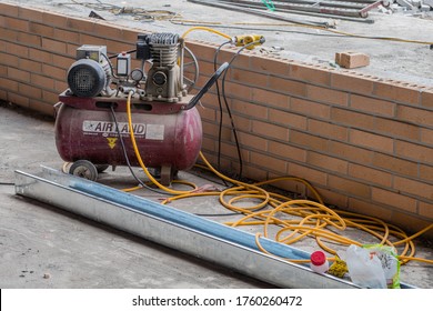 Cheongju, South Korea; May 31, 2020: Portable air compressor and hoses in front of brick wall at construction site.