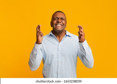 Cherished wish. Mature african american man crossing his fingers with great hope, orange studio background