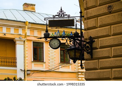 Chernivtsi, Ukraine-May 13,2021:Scenic advertising sign on the building corner. Detailed view of sign plate which decorated by street clock and colored bottles.Facade of building in the background.