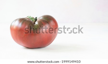 Cherokee purple is a very old variety tomato, also known as 	beefsteak. The tomato is lying on a white table in the rays of sunlight - close-up and copy space