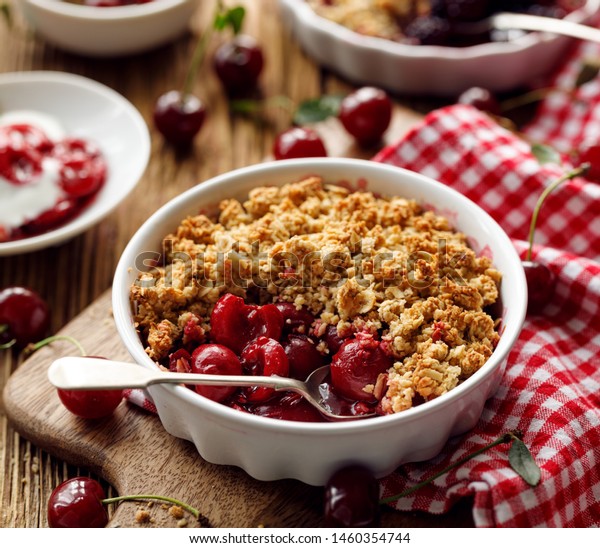 Cherry crumble, stewed fruits topped with\
crumble of oatmeal, almond flour, butter and sugar  in a baking\
dish on a wooden table,\
close-up