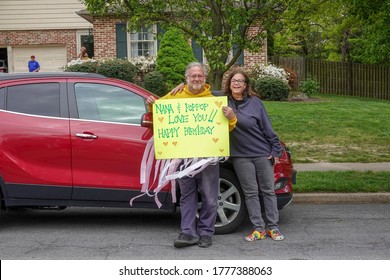 Cherry Hill, New Jersey - July, 2020: Grandparents Hold Up A Decorated Happy Birthday Sign For Their Grandchild At A Distance While Leaning On A Red Car