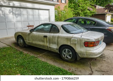 Cherry Hill, New Jersey - July, 2020: Side view of an extremely dirty white car with a flat front tire in a driveway in front of a white garage door