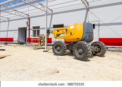 Cherry Picker Parked Next To A Newly Painted Metal Frame Building.