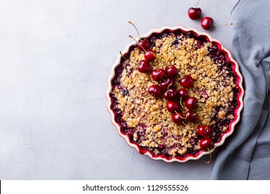 Cherry, red berry crumble in baking dish. Grey background. Top view. Copy space.