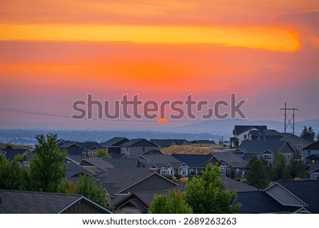 A cherry red sun disappears behind the mountains above the city of Spokane Washington at sunset.