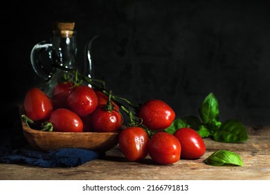 Cherry tomatoes on wooden board with fresh basil leaves and olive oil bottel at the background - dark and moody