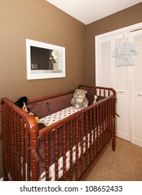 Cherry Wood Baby Crib In Nursery Interior With Brown Wall.