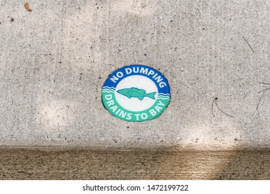 Chesapeake City, MD - May 19, 2019: Sidewalk Curb Above Storm Sewer Drain With Blue And Green Medallion With A Fish On It And The Words 