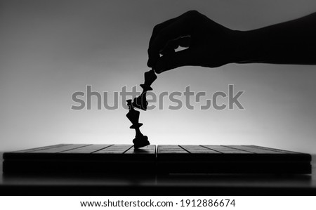 Chess board with chess pieces silhouettes on white background. Concept of business ideas, competition and strategy ideas. Black and White classic art photo. Chess player hand. Weak king was defeated