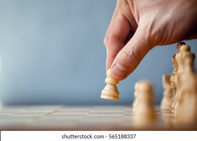 Chess game player makes a move the white pawn one step forward. Chess pieces on the board on blue background. Chessman playing chess and makes the first move a pawn, and showing the hand. 