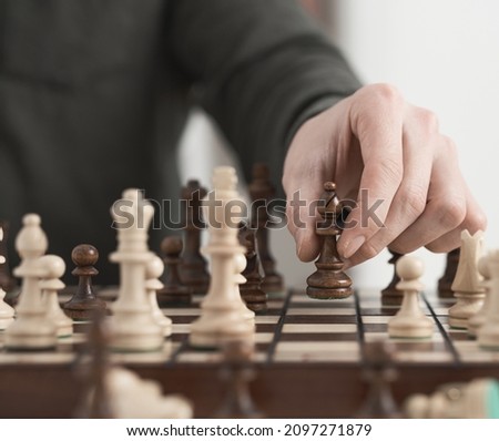 Chess game. The young player makes a move with the queen-officer piece. Wooden chess chessboard brown color. Game of chess
             