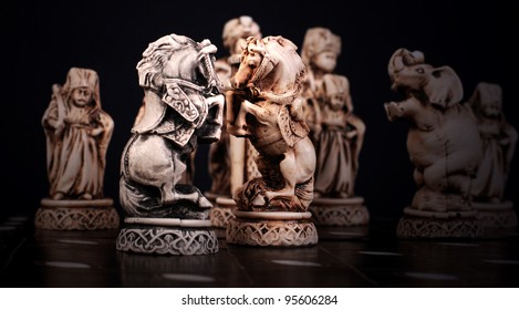 Chess pieces stylized like mini sculptures on the chessboard. White and black horses.