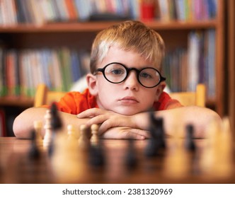 Chess, thinking or bored with a boy student learning how to play a boardgame at school for education. Face, strategy and glasses with a young student child in a classroom for intelligence development