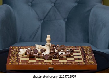 A Chessboard On Which Stands A White Queen And All The Other Defeated Pieces Of Wood Lie Around. An Iron Table And A Comfortable Chair In The Living Room Where The Game Of Chess Takes Place.