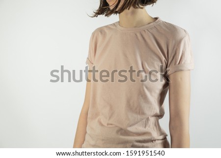 Chest body part of a female person in neutral background. Woman in simple t-shirt standing in studio background