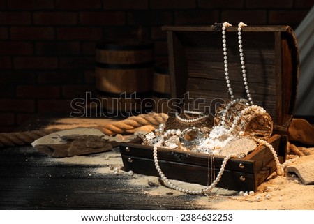 Chest with treasures and scattered sand on wooden table, space for text