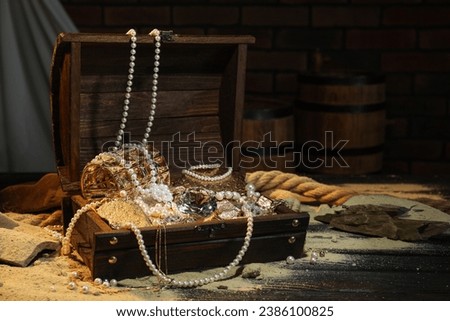 Chest with treasures and scattered sand on wooden table, space for text