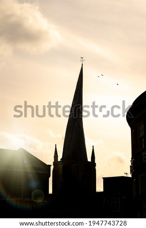 Chesterfield Crooked Spire church silhouette of tower in town centre with sun setting behind and birds in sky cockerel weather vein on top. Historic St Marys parish worship building.