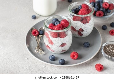 Chia pudding with blueberry and raspberry in two glass jars on light gray background. Healthy food, High angle