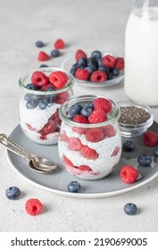Chia pudding with blueberry and raspberry in two glass jars on gray background. Healthy food