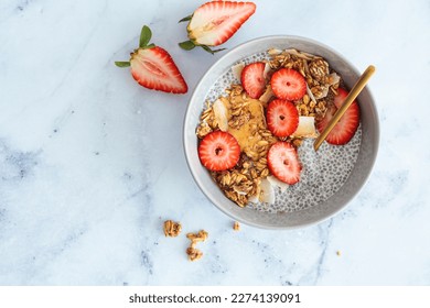 Chia pudding with homemade coconut granola, peanut butter and strawberries in gray bowl, marble background, top view. Healthy plant based diet, detox, summer recipe. - Powered by Shutterstock