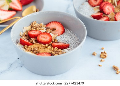Chia pudding with homemade coconut granola, peanut butter and strawberries in gray bowl, marble background. Healthy plant based diet, detox, summer recipe. - Powered by Shutterstock