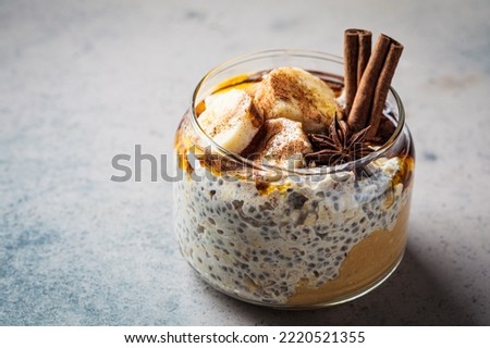 Chia pudding jar with banana, peanut butter, cinnamon and maple syrup, dark background, copy space. Winter breakfast concept.