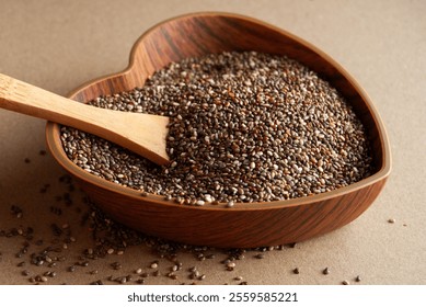 Chia seeds in a heart-shaped wooden bowl with a wooden spoon.