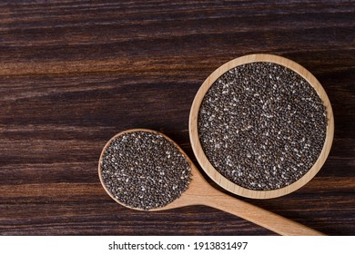 Chia seeds ( Salvia hispanica ) in wooden bowl and spoon isolated on wooden table background. Top view. Flat lay.