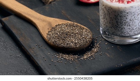Chia seeds in a wooden spoon on a black table, close up