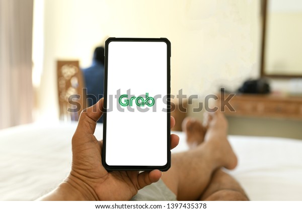 Chiang Mai,\
Thailand - 15 May 2019:The hand holding the Huawei Mate 20x\
smartphone the App Grap screen show.Him lying on the bed in the\
hotel and using  App to pick up the\
car.