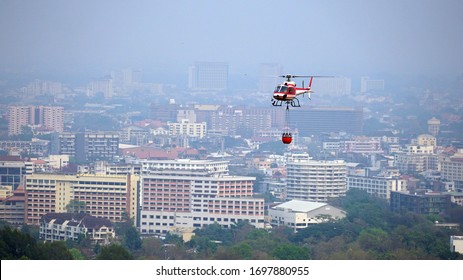 Chiang Mai, Thailand - April 8, 2020: Eurocopter AS350 Helicopter carries water flying over Chiang Mai City to douse forest fires on Doi Suthep mountain