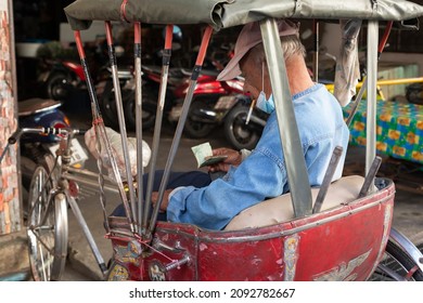 Chiang Mai, Thailand - December 14, 2021 : Unidentfied elderly man counting banknotes of small value on the passenger seat of a hired tricycle at Chiang Mai, Thailand.