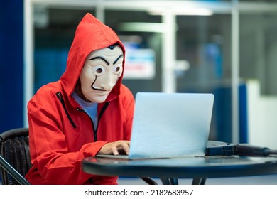 Chiang Mai, Thailand – July 23, 2022 : Hacker In The Office, Person Wearing Red Costume With Iconic Dali Face Mask From The Series TV Money Heist, La Casa De Papel Stealing Data From Computer