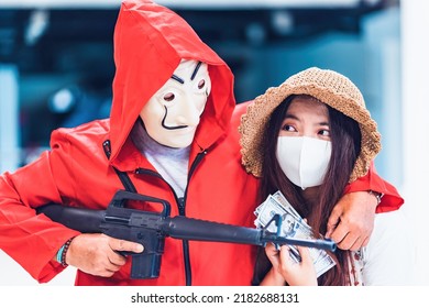 Chiang Mai, Thailand – July 23, 2022 : Terrorist Wearing Red Costume With Mask Holding Gun Kidnapping Young Women For A Hostage In Abandoned Building. The Series TV Money Heist, La Casa De Papel 