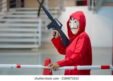 Chiang Mai, Thailand – July 23, 2022 : Person With Weapon And Red Costume With Iconic Dali Face Mask From The Series Money Heist, La Casa De Papel In Masks From The Popular Series. A Crew Of Criminals