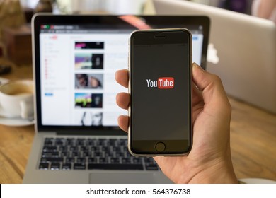 CHIANG MAI,THAILAND - JAN 26, 2017: A woman showing screen shot of Youtube on iphone 6s. YouTube app on the screen lying on old wood desk. YouTube is the popular online video sharing website.