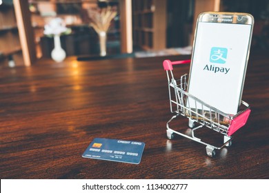CHIANG MAI,THAILAND - July 7,2018: Mobile Phone using Alipay app on the screen in shopping cart and credit card on wooden table.