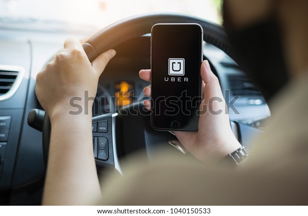 CHIANG MAI,THAILAND -\
MARCH 01, 2018 : A uber driver hand holding Uber app showing on\
iPhone 6s on road and black car, Uber is smartphone app-based\
transportation network.
