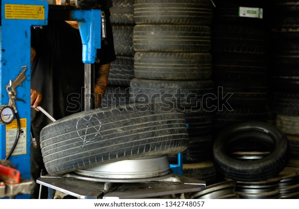 Chiang rai, Thailand - March 18,2019:The\
mechanic wears a black short-sleeved shirt, a left arm with a\
tattoo, removing the tire from the\
wheel.